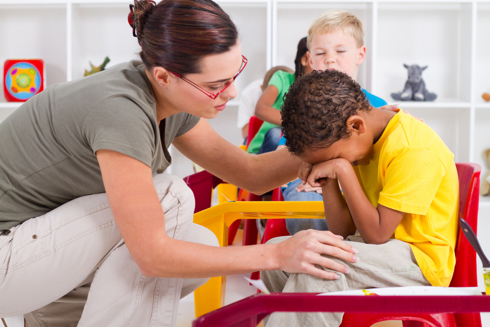 TeacherComfortingCryingPreschoolBoy Teacher comforting a crying preschool toddler in a classroom setting