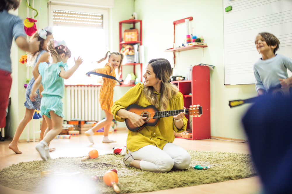MomentOfHappinessChildrenWithTeacherInPreschool Preschool teacher interacting with young children during a classroom activity, showing a positive and supportive learning environment.