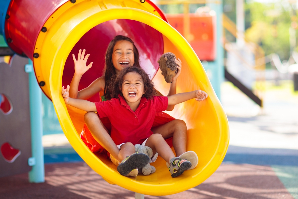 KidsOnPlaygroundChildrenPlayOutdoorOnSchoolYardSlide Preschool-aged children playing together on a playground during an outdoor summer camp program.