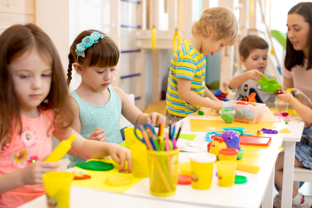 GroupOfPreschoolKidsEngagedInHandcraftsChildrenAndTeacher Group of preschool children engaged in hands-on craft activity in a classroom, developing creativity and learning skills.