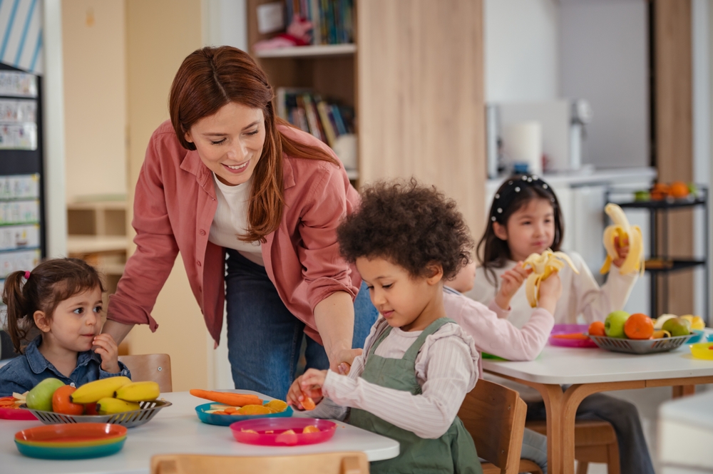 PreschoolTeacherHelpsADiverseGroupOfYoungChildrenDuring Preschool teacher guiding a diverse group of young children during an interactive classroom learning activity.
