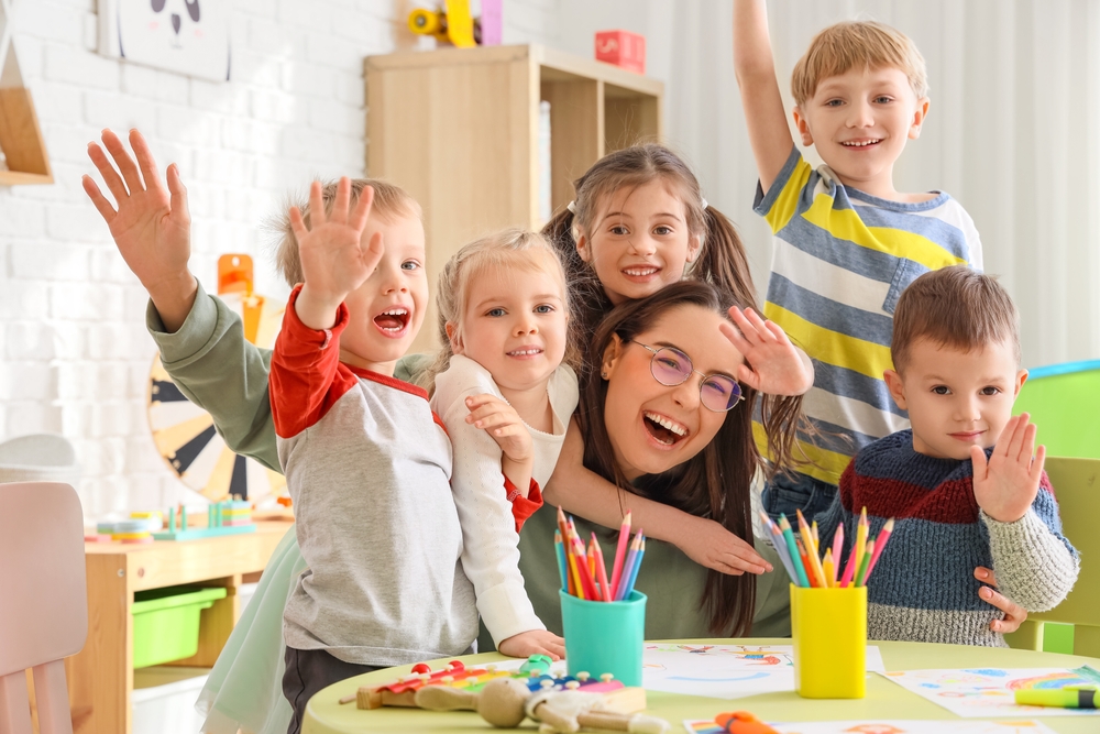 CuteLittleChildrenHuggingNurseryTeacherInKindergarten Preschool children hugging their teacher in a classroom