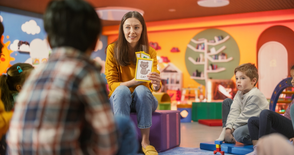 BeautifulDaycareTeacherLearningAlphabetWithYoungTalentedKidsFemale Preschool teacher helping young children learn the alphabet in a classroom